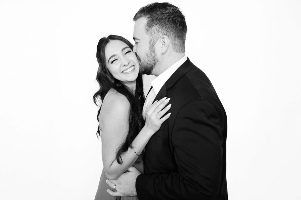 Black-and-white portrait of a joyful couple dressed in formal attire, photographed with studio lighting inside a modern Phoenix wedding photo booth.